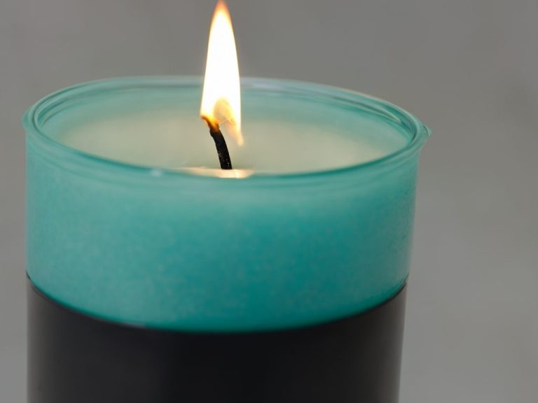 Brennder Kerze mit grünem Glasbehälter und schwarzem Fuß auf grauem Hintergrund.